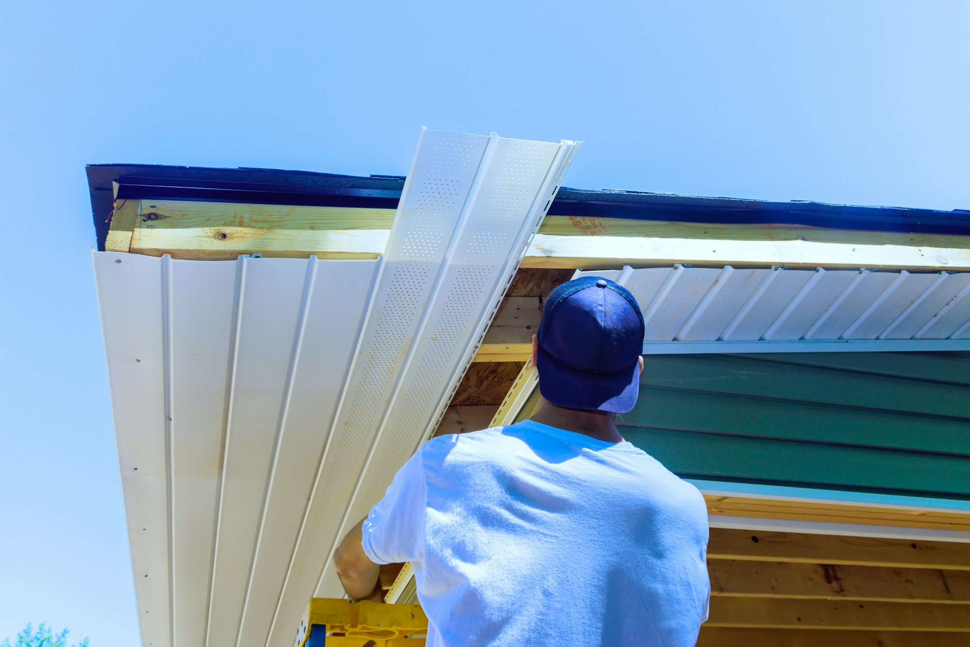 Mounting vinyl soffit plastic boards to roof rafters on a ceiling house