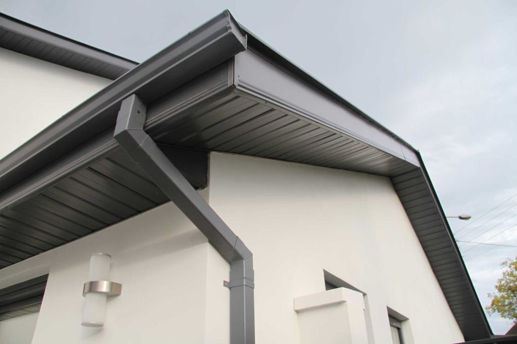 Close-up of new black gutters and downspouts installed on a modern white home in Loveland, CO