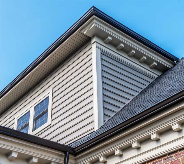 Close-up of residential siding, soffit, fascia, and roofline on a modern home under a clear blue sky.