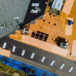 A roofer nailing shingles with air gun, replacing roof cover protection being applied
