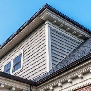 Close-up of residential siding, soffit, fascia, and roofline on a modern home under a clear blue sky.